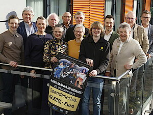 Menschen stehen auf einem Balkon und halten ein Plakat in der Hand. Darauf steht: Spendenerlöse 42.520 Euro.